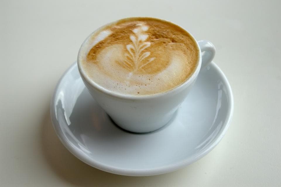 A cappuccino with latte art in a white cup and saucer