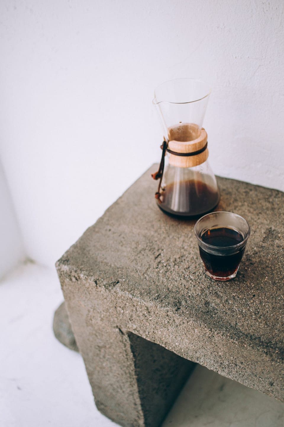 A glass coffee carafe and a short glass of filter coffee on a concrete block