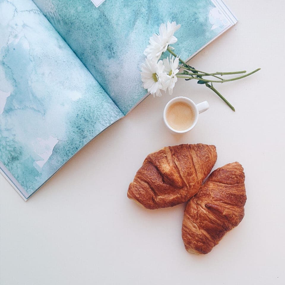 Two croissants, a small coffee and white flowers on a pale table