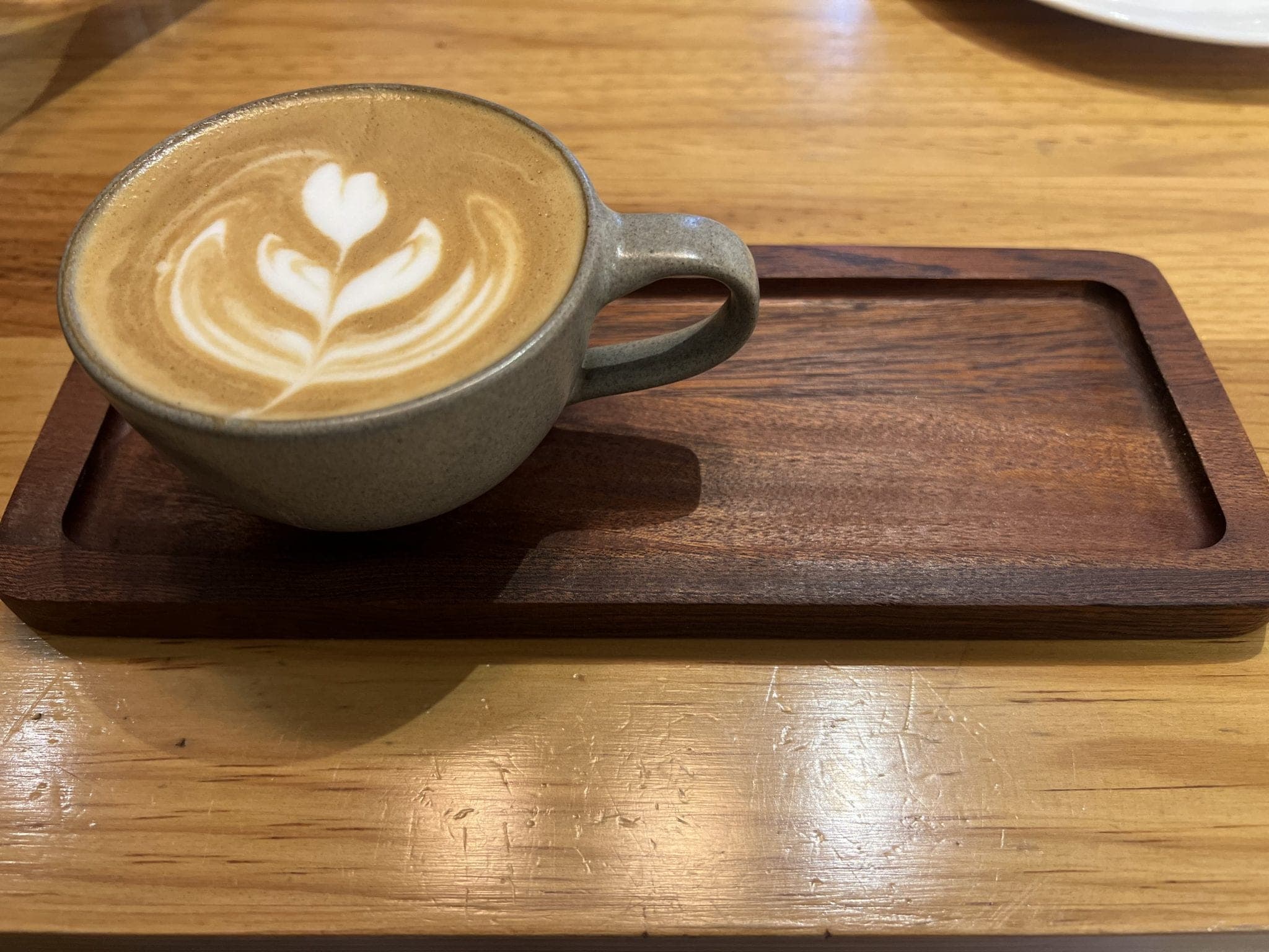 A latte with rosetta latte art in a stoneware cup on a walnut tray