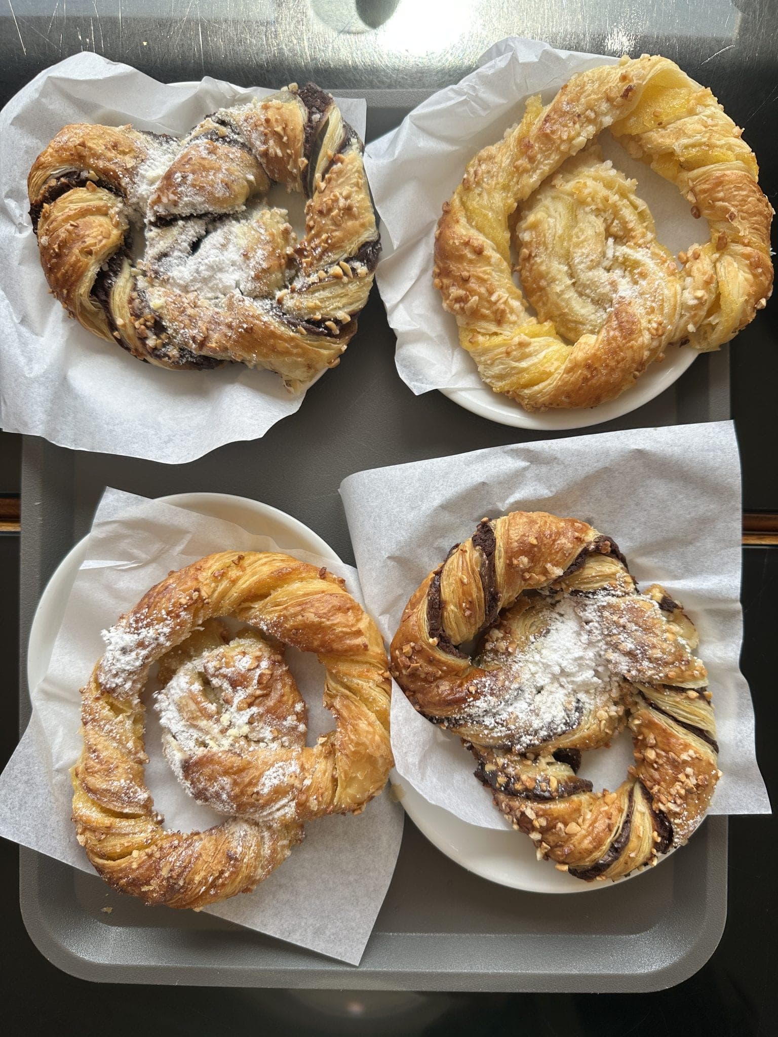 Four twisted pastries dusted with sugar on paper-lined plates