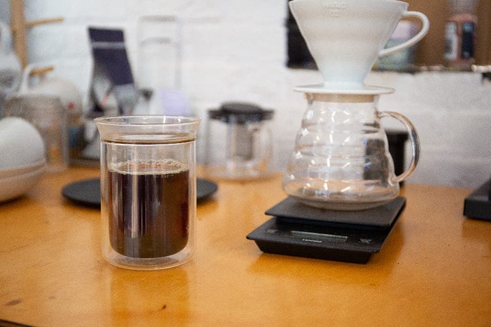 A pour-over station with a dripper, glass server and scale on a wooden counter